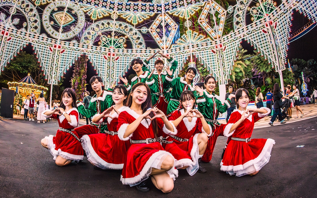 Performers in festive costumes at Gardens by the Bay, Singapore, with illuminated decorations.