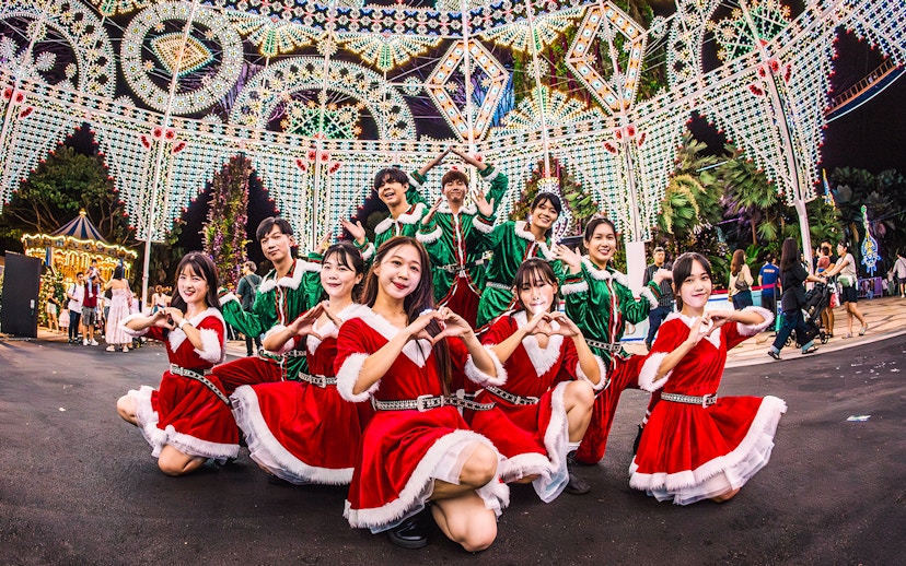 Performers in festive costumes at Gardens by the Bay, Singapore, with illuminated decorations.