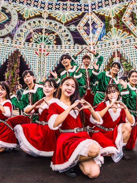 Performers in festive costumes at Gardens by the Bay, Singapore, with illuminated decorations.
