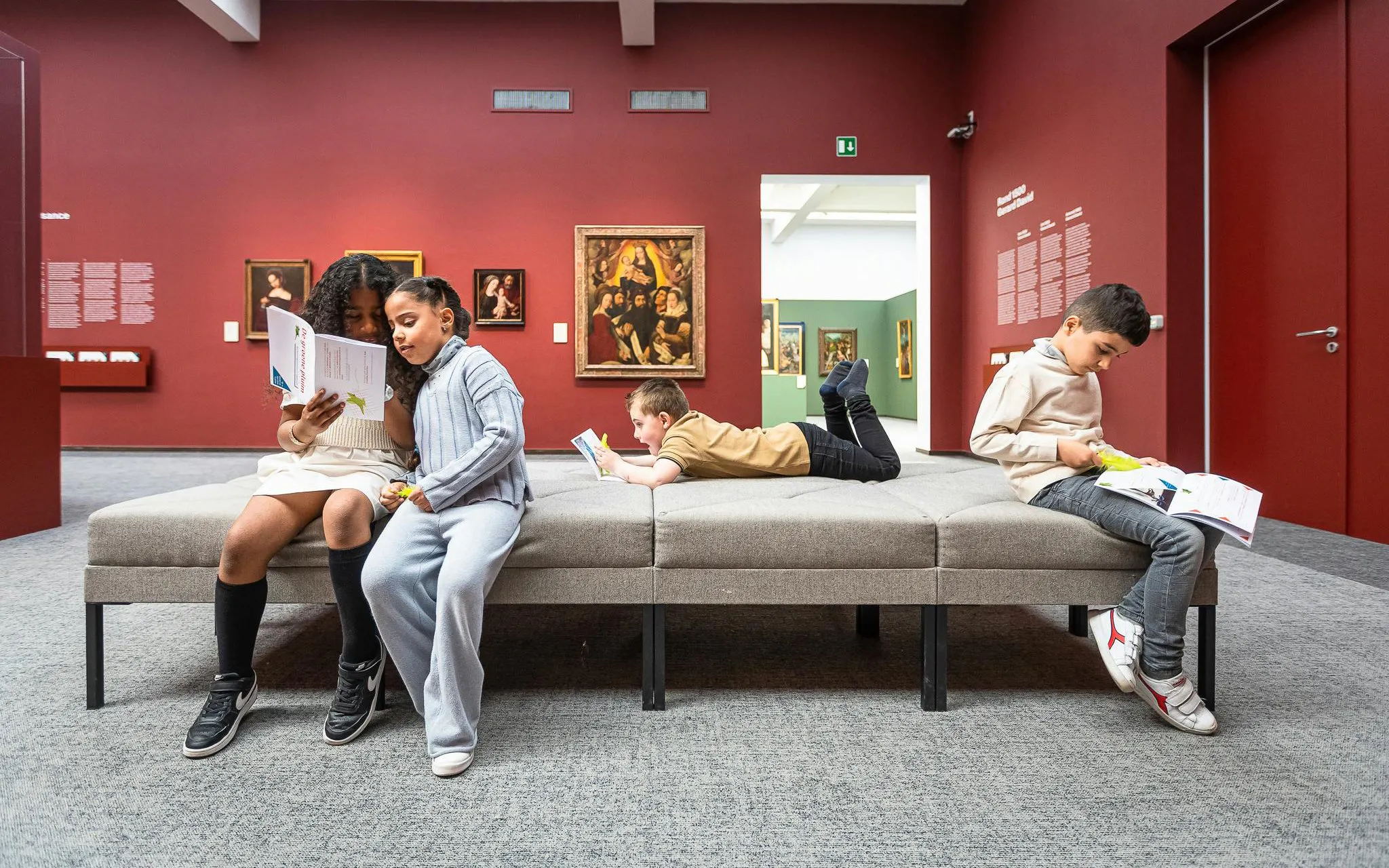 Children reading in Groeningemuseum gallery with paintings in the background.