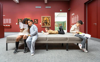 Children reading in Groeningemuseum gallery with paintings in the background.