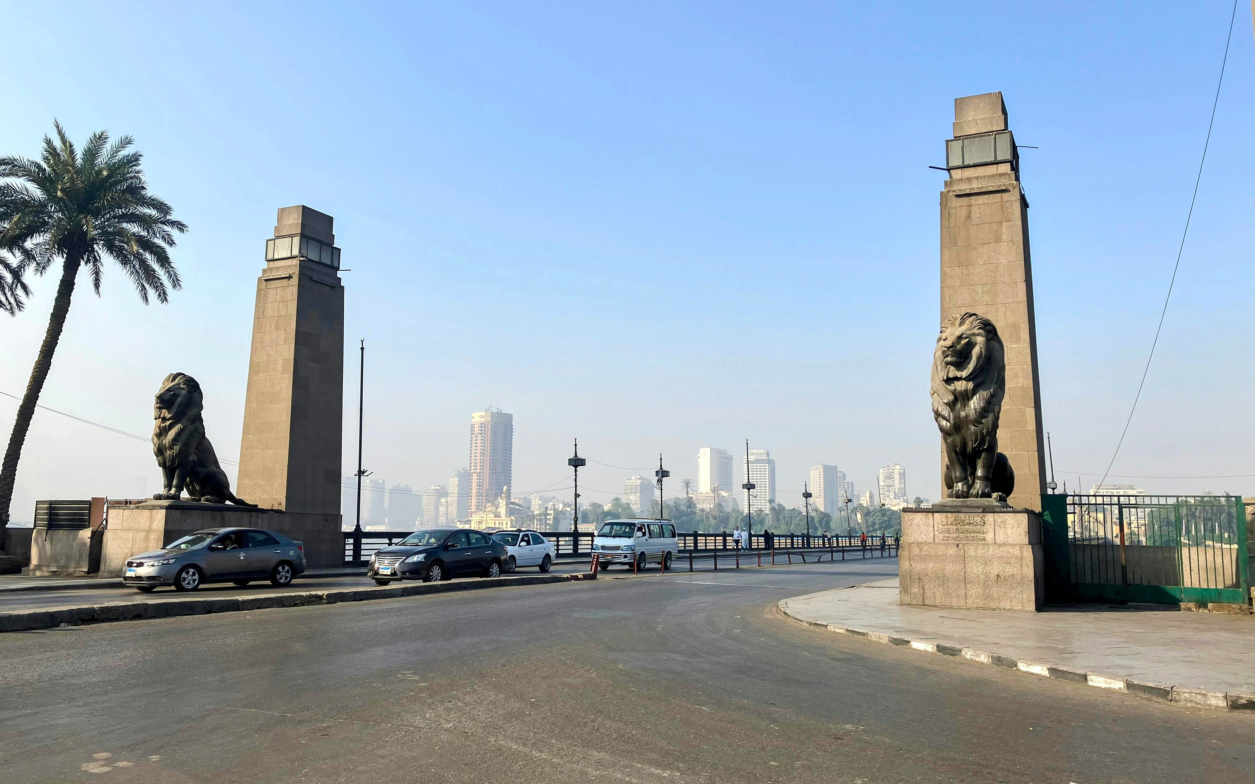 Qasr El Nil Bridge entrance with lion statues and city skyline in Cairo, Egypt.