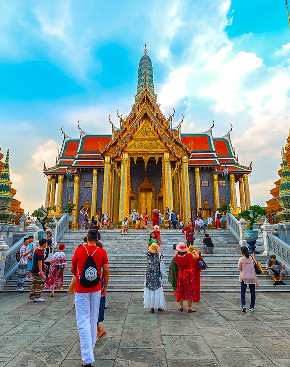 Visitors exploring the ornate entrance of the Grand Palace in Bangkok, Thailand.