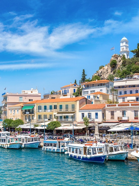 Boats docked along the waterfront in Poros, Greece, with hillside houses and a clock tower.
