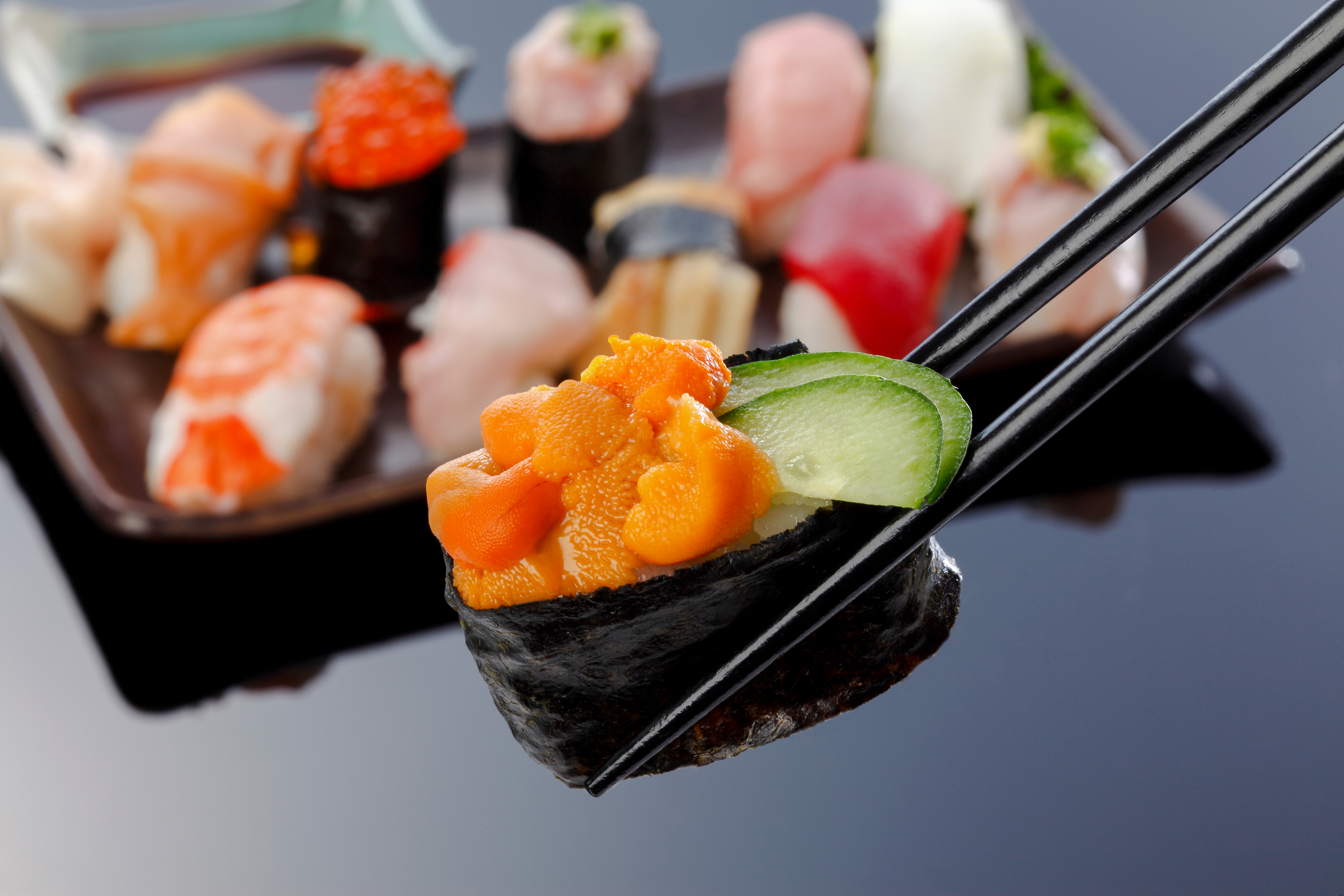 Chopsticks holding sea urchin sushi (uni) with cucumber slice.