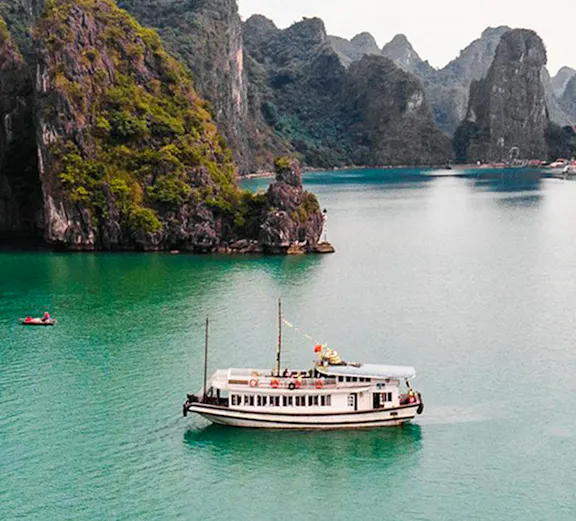 Cruise ship sailing in Ha Long Bay's emerald waters, surrounded by limestone islands.