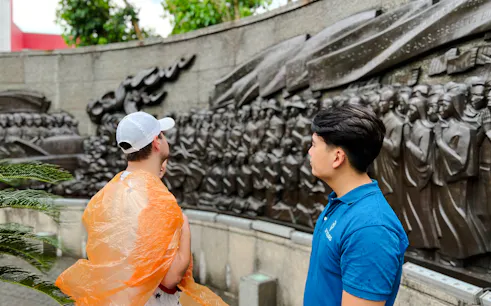 Visitors observing a historical relief sculpture in Ho Chi Minh City on a scooter day tour.