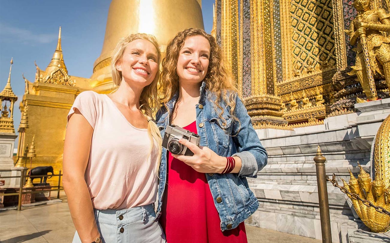 Visitors at the Grand Palace in Bangkok with ornate golden temple backdrop.