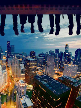 Feet dangling over Chicago skyline at dusk, showcasing city skyscrapers and lights.