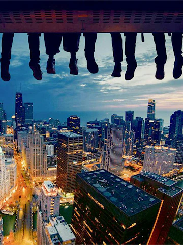 Feet dangling over Chicago skyline at dusk, showcasing city skyscrapers and lights.