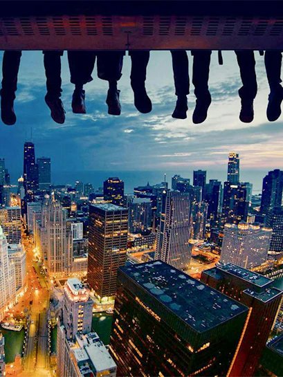 Feet dangling over Chicago skyline at dusk, showcasing city skyscrapers and lights.