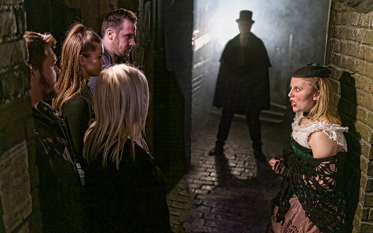 Visitors in a dimly lit alley encounter a Jack the Ripper figure at London Dungeon.