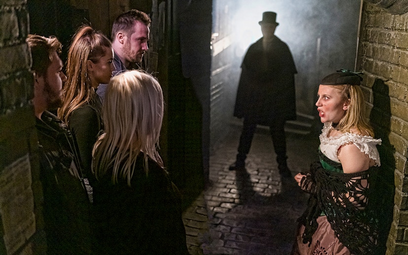 Visitors in a dimly lit alley encounter a Jack the Ripper figure at London Dungeon.