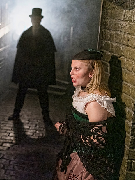 Visitors in a dimly lit alley encounter a Jack the Ripper figure at London Dungeon.