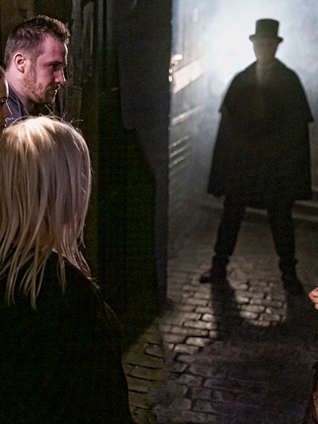 Visitors in a dimly lit alley encounter a Jack the Ripper figure at London Dungeon.