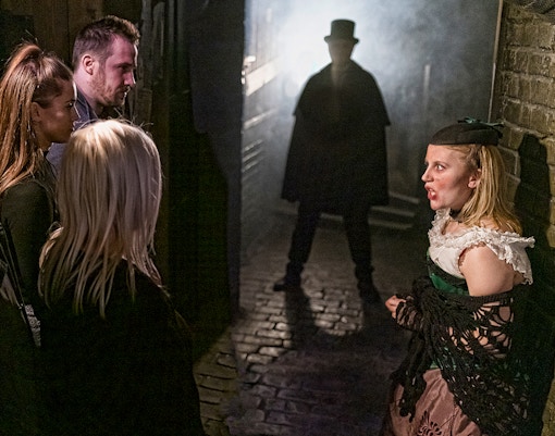 Visitors in a dimly lit alley encounter a Jack the Ripper figure at London Dungeon.
