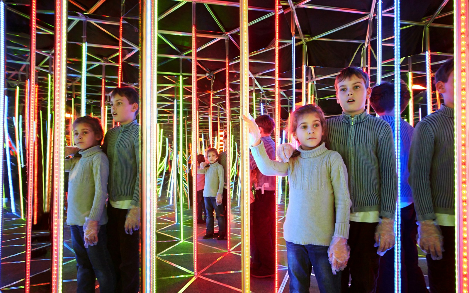 Children exploring a colorful mirror maze with reflections.