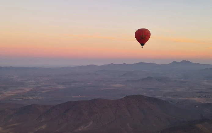 Hot air balloon over Marrakesh landscape at sunrise.