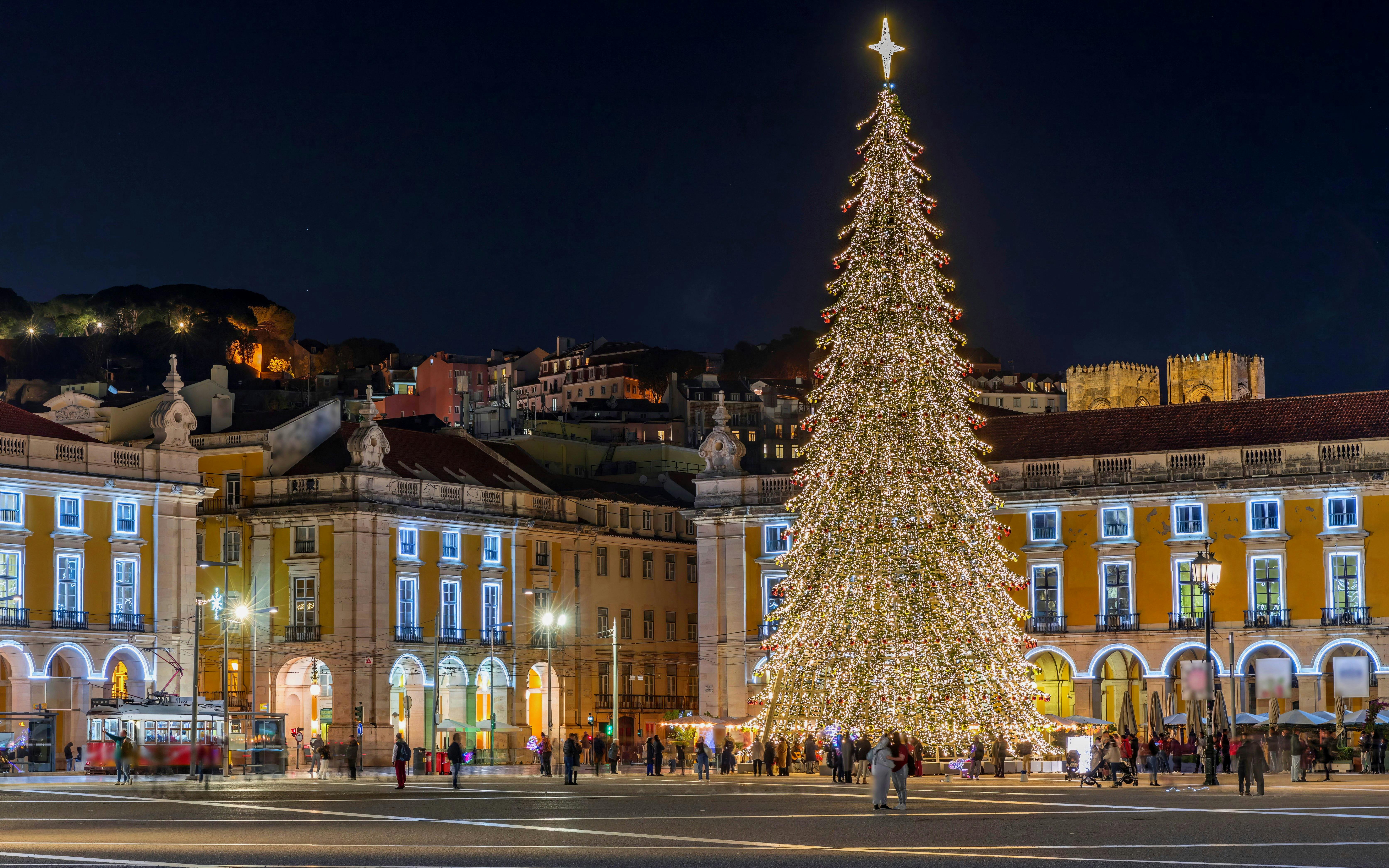 Commerce Square in Lisbon with a large Christmas tree and crowds celebrating at night, Portugal.