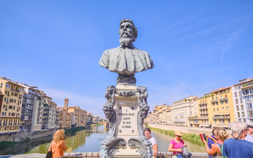 Bust of Benvenuto Cellini on Ponte Vecchio, Florence, with tourists and river view.