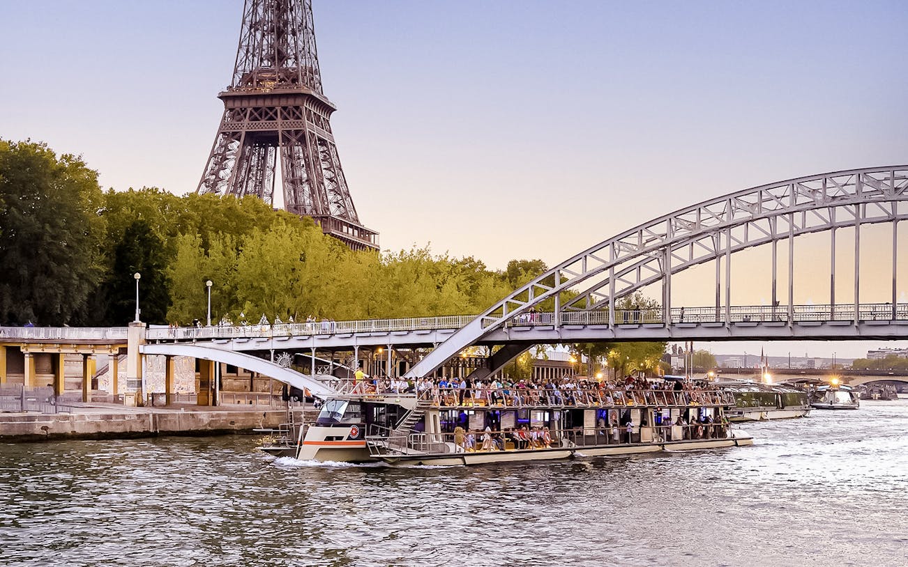 Seine River cruise boat near Eiffel Tower at sunset, Paris.