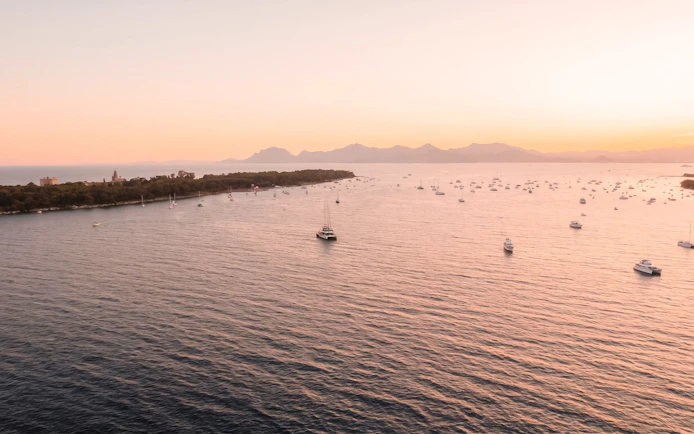 Boats on the water during sunset in the French Riviera, with distant mountains.