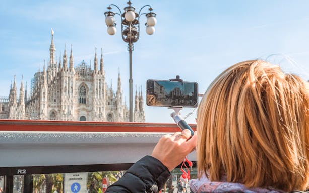 Hop-on hop-off bus view of Milan Cathedral, tourist capturing photo.