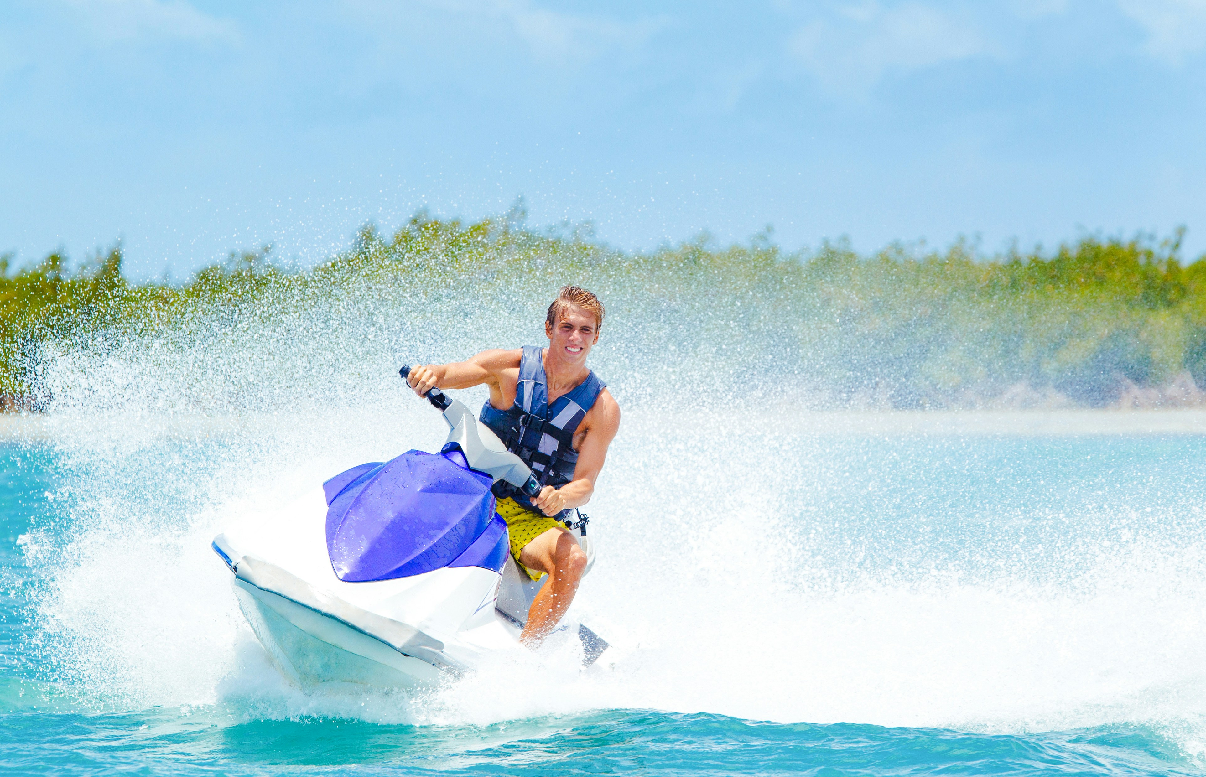 Man riding jet ski on turquoise ocean near tropical island.