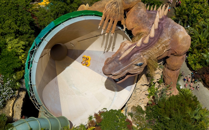 Riders on Cyclone slide with dragon at Siam Park, surrounded by lush greenery.