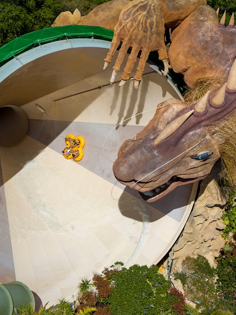 Riders on Cyclone slide with dragon at Siam Park, surrounded by lush greenery.
