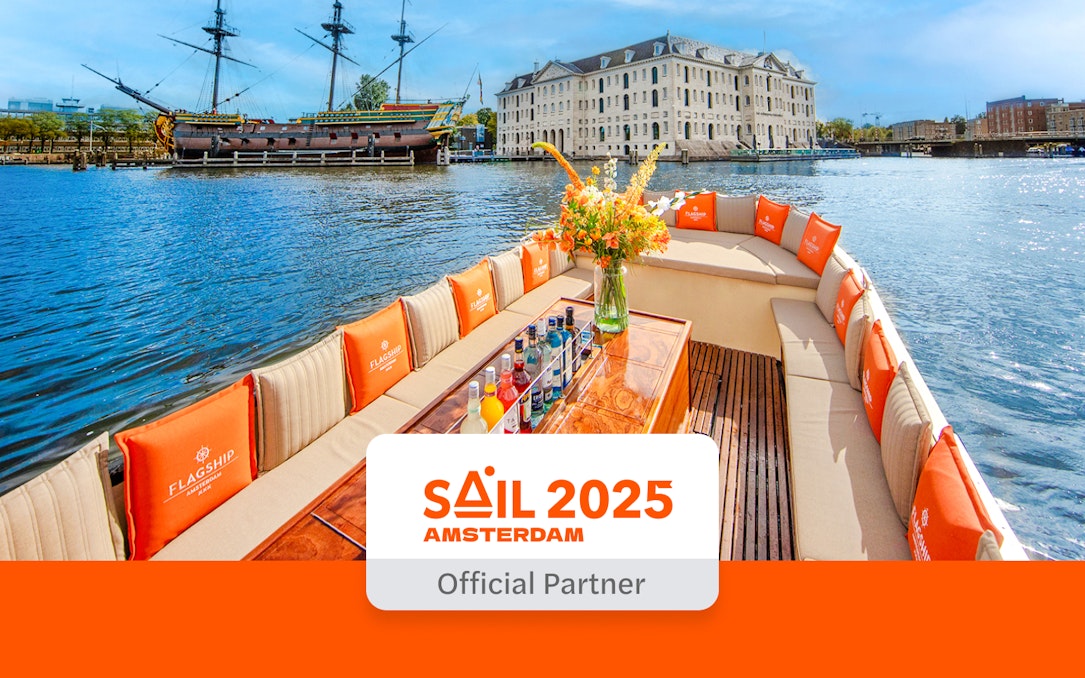 Boat tour with drinks on Amsterdam canal near historic ship and building, SAIL Amsterdam 2025.