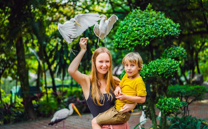 Woman and child interacting with birds at Bali Bird Park.