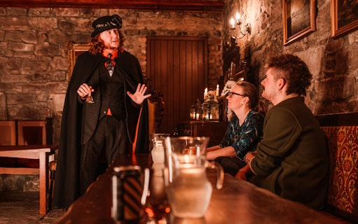 Tour guide in period costume leading an evening underground ghost tour in Edinburgh.
