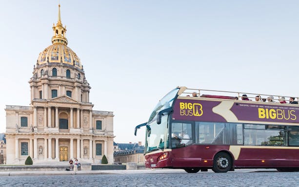 Big Bus Paris tour passing Les Invalides with tourists on board.