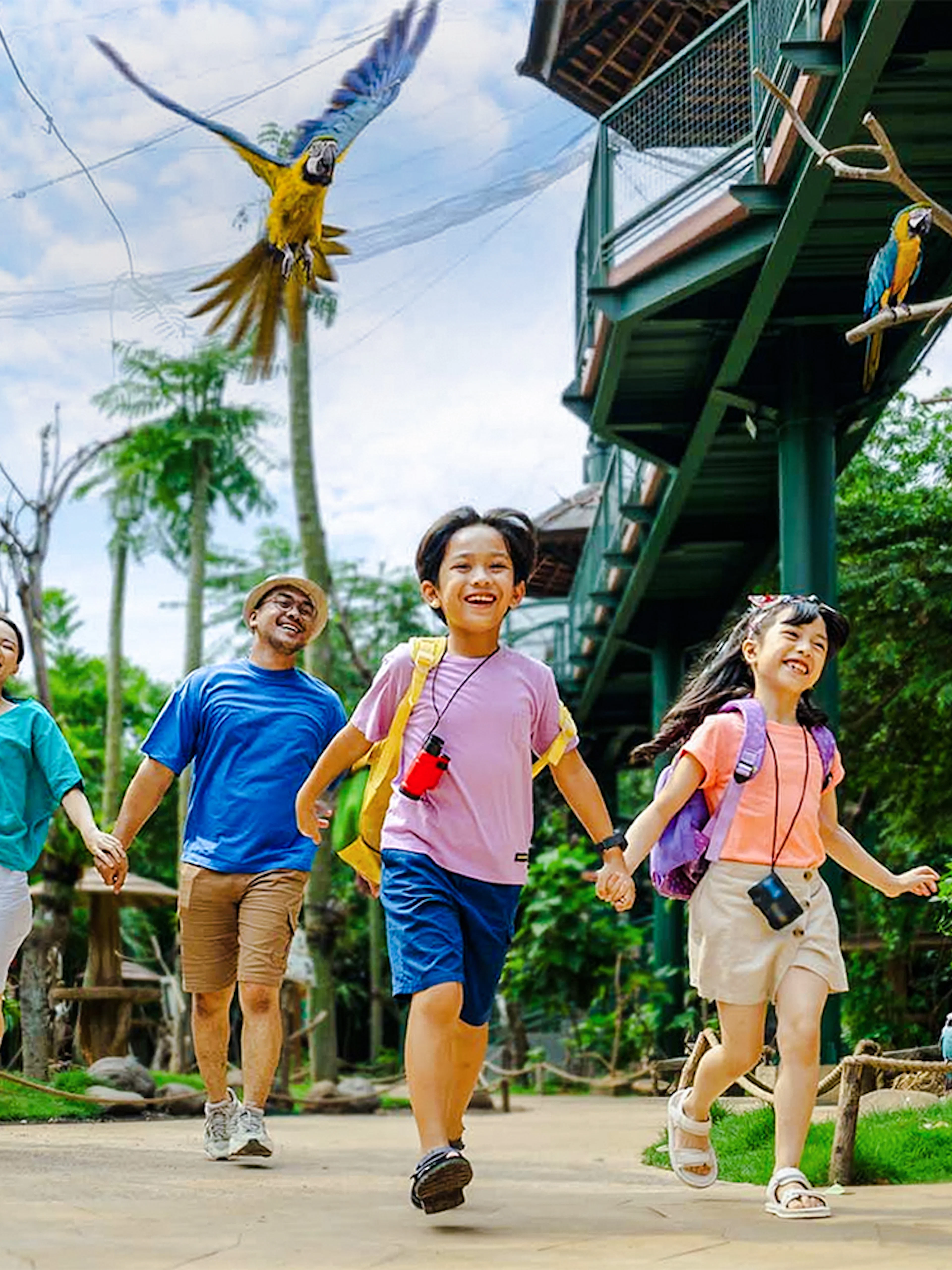 Children enjoying a walk at Jakarta Bird Land with colorful parrots flying above.