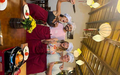 Group cooking class participants in Hoi An wearing chef hats and aprons, holding knives.