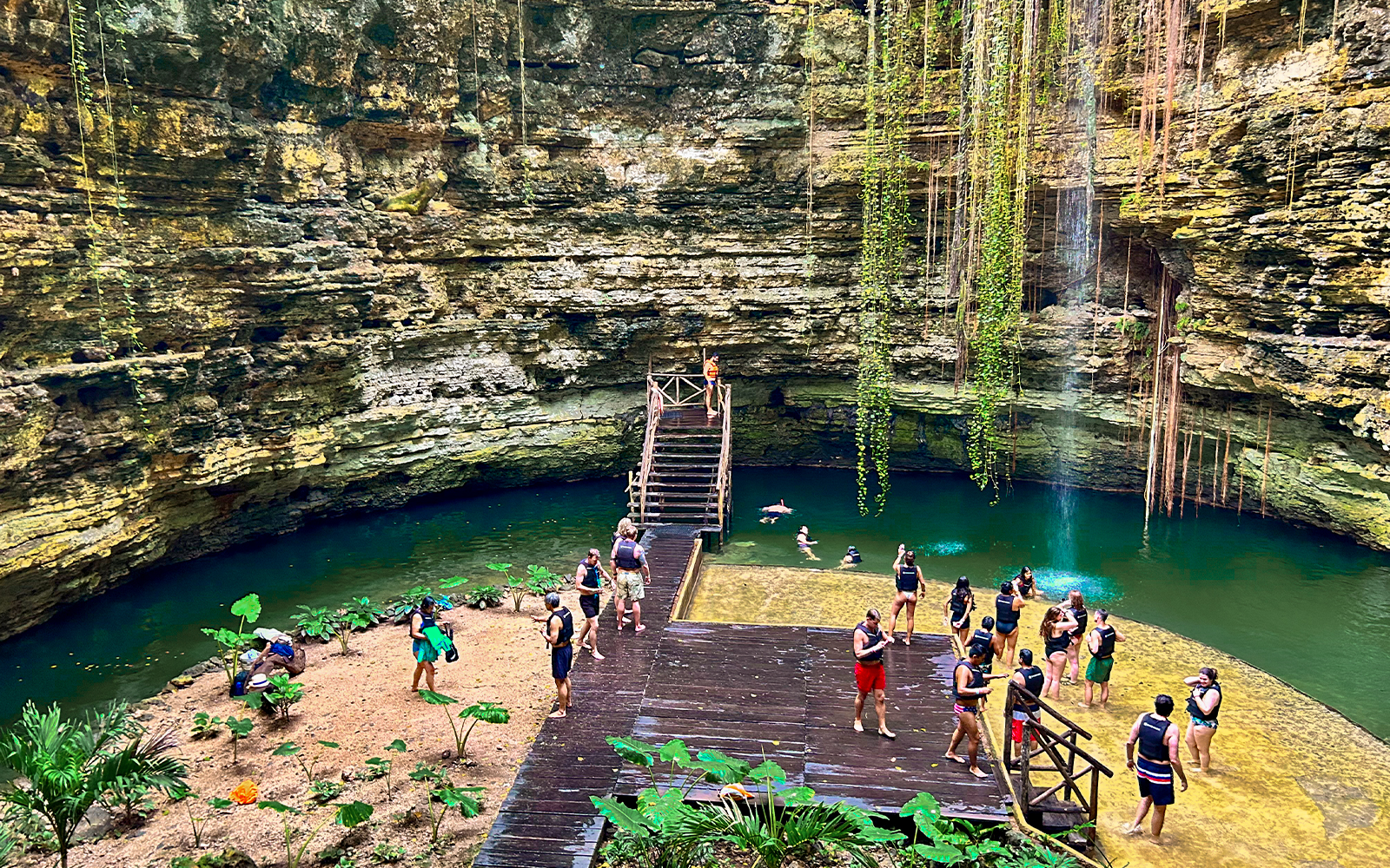 Tourists swimming and relaxing at a cenote with lush greenery and rock formations.