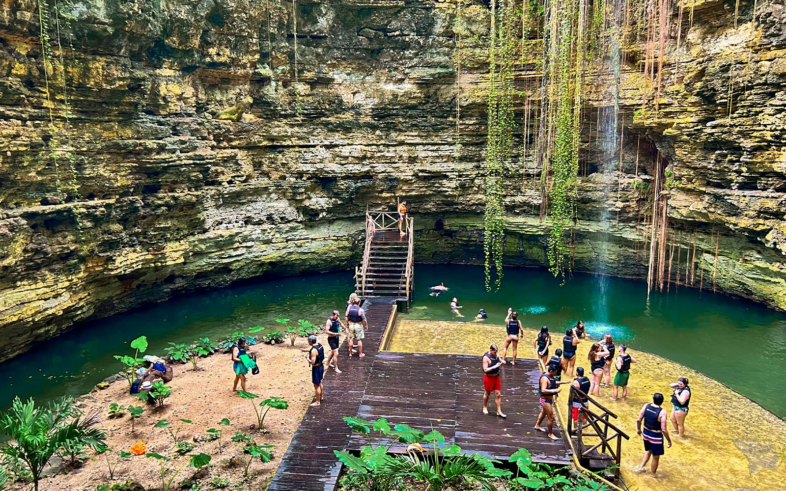 Tourists swimming and relaxing at a cenote with lush greenery and rock formations.