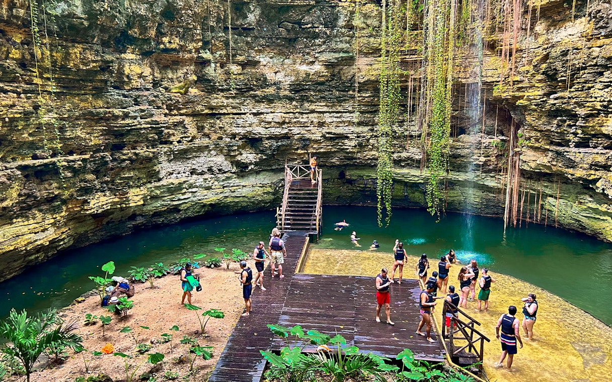 Tourists swimming and relaxing at a cenote with lush greenery and rock formations.