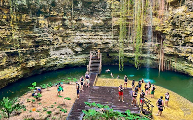Tourists swimming and relaxing at a cenote with lush greenery and rock formations.