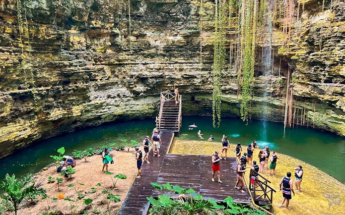 Tourists swimming and relaxing at a cenote with lush greenery and rock formations.