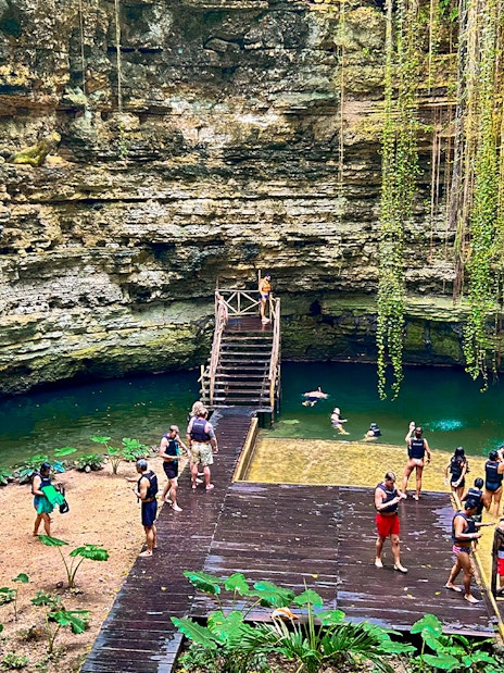 Tourists swimming and relaxing at a cenote with lush greenery and rock formations.