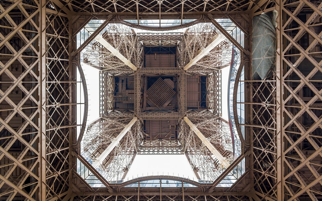 View from beneath the Eiffel Tower's intricate iron structure during guided elevator tour.