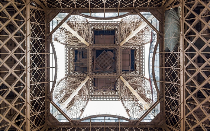 View from beneath the Eiffel Tower's intricate iron structure during guided elevator tour.