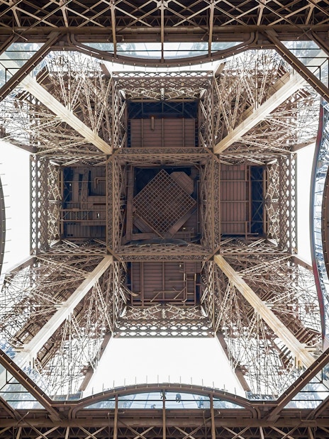 View from beneath the Eiffel Tower's intricate iron structure during guided elevator tour.