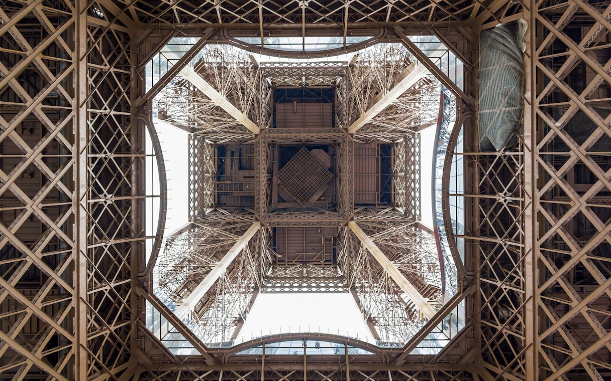 View from beneath the Eiffel Tower's intricate iron structure during guided elevator tour.