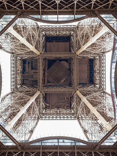 View from beneath the Eiffel Tower's intricate iron structure during guided elevator tour.