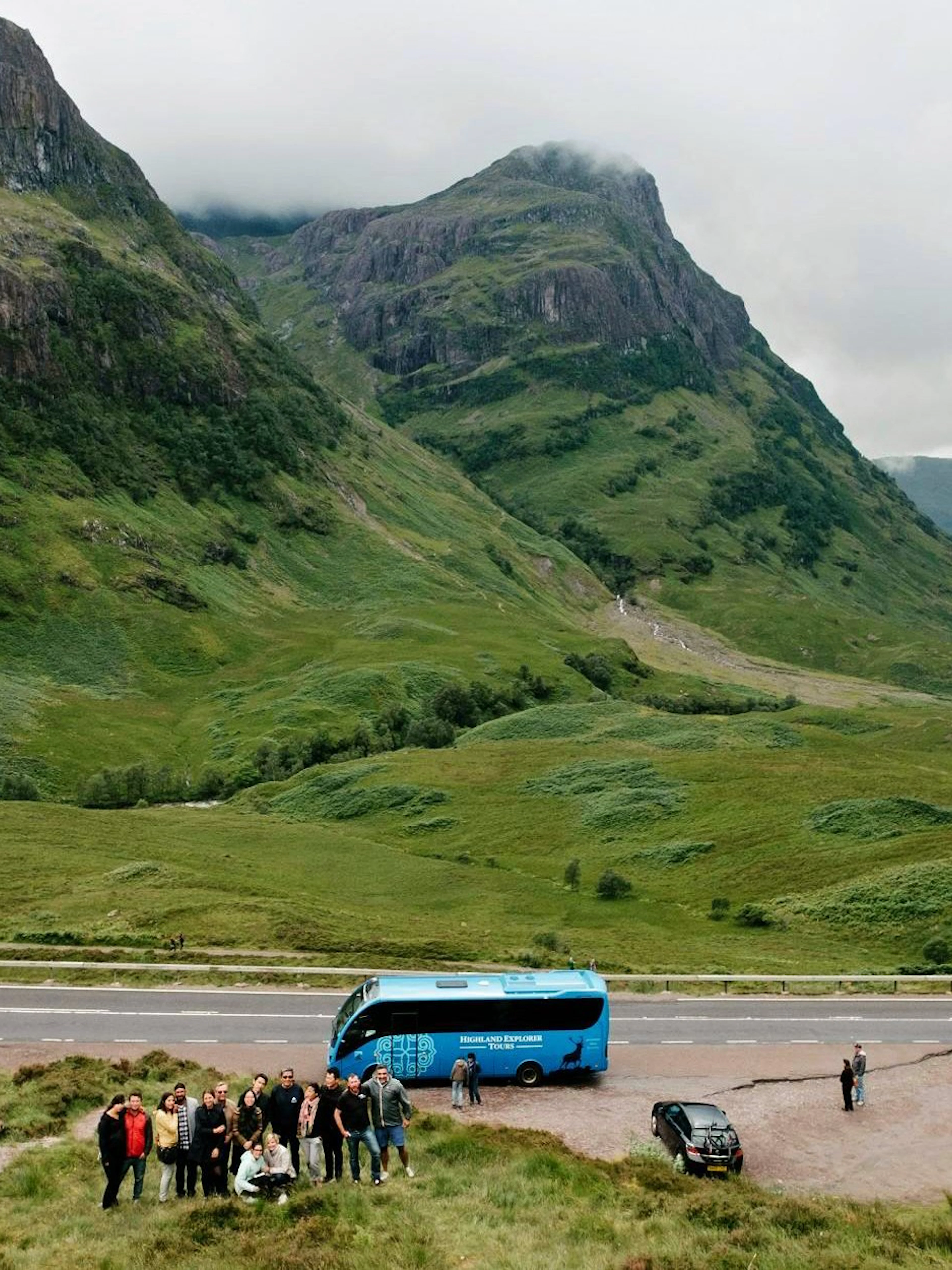 Tour group with bus in the Scottish Highlands, surrounded by lush green mountains.