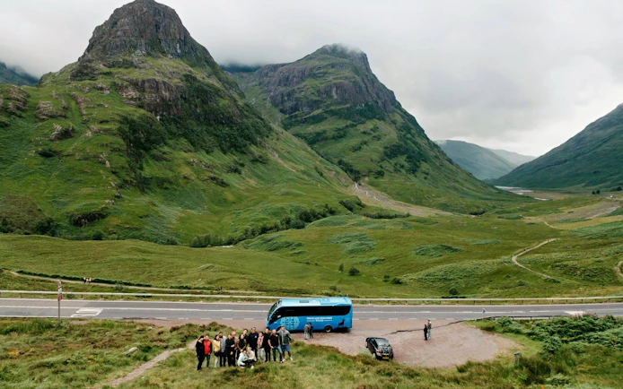 Tour group with bus in the Scottish Highlands, surrounded by lush green mountains.