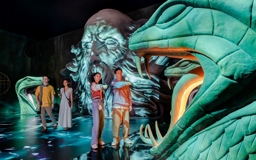 Visitors exploring a magical chamber with large serpent statues at Harry Potter Visions of Magic.